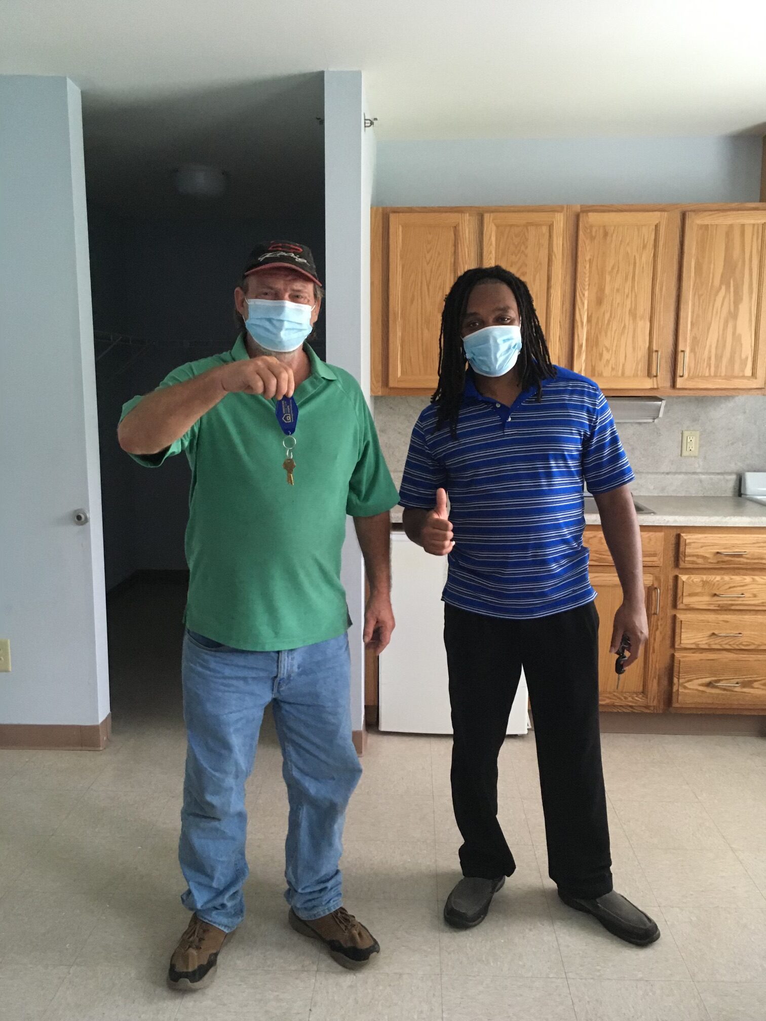 Jeffrey and Phillip in an empty apartment. Jeffrey is holding up house keys while Phillip makes a thumbs up.