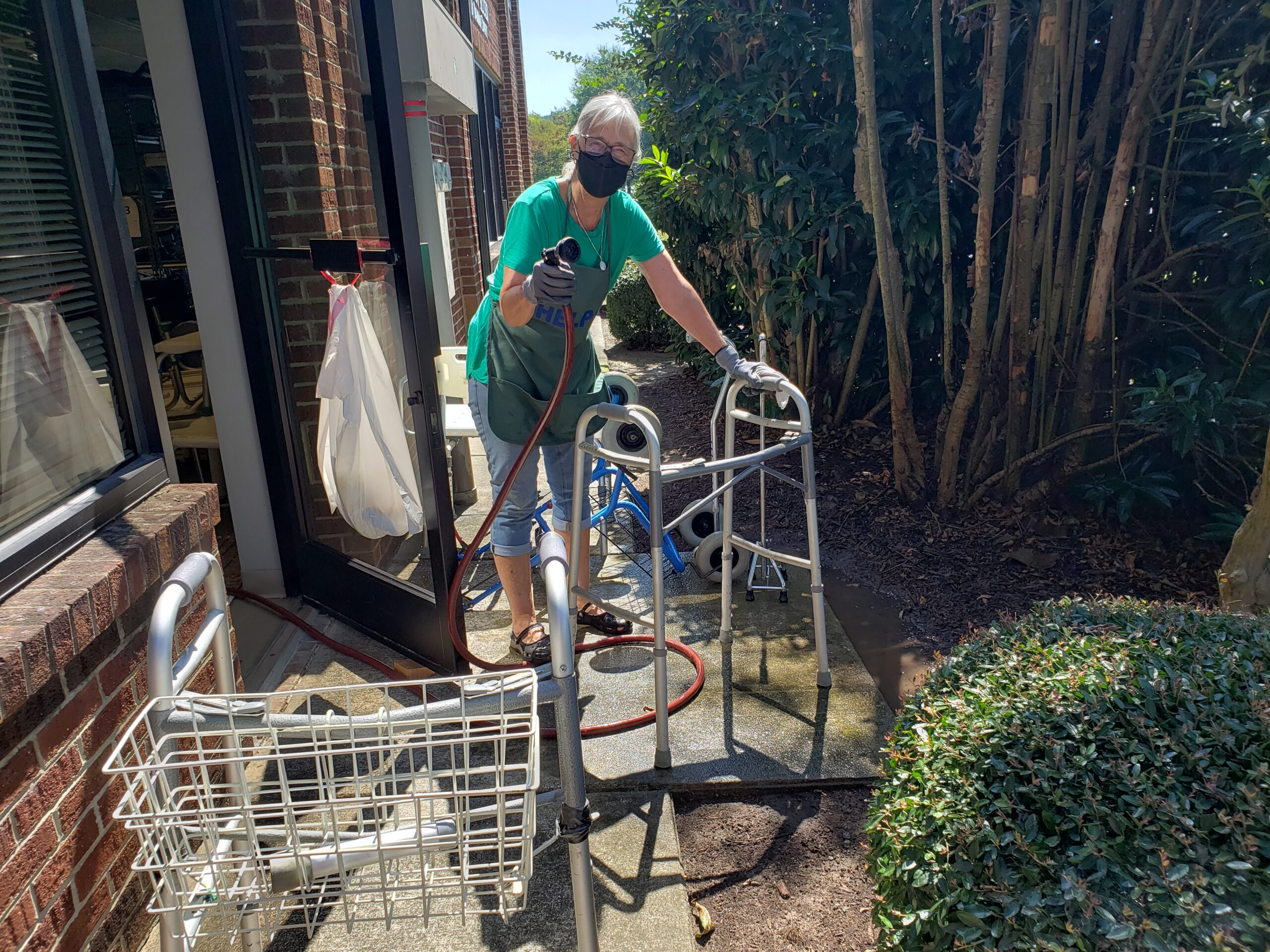 A volunteer washing a walker outside, pointing the garden hose at the camera. 